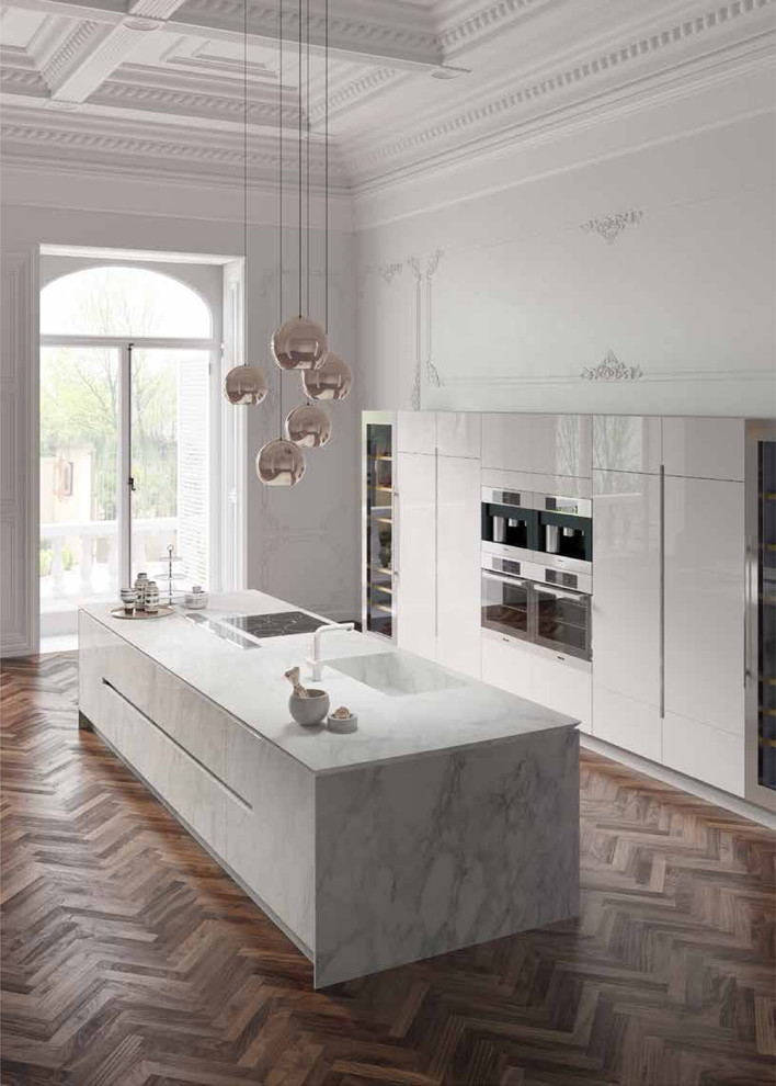 Idéer för att renovera ett mycket stort funkis linjärt kök med öppen planlösning, med en integrerad diskho, släta luckor, vita skåp, marmorbänkskiva, integrerade vitvaror, mellanmörkt trägolv och en köksö