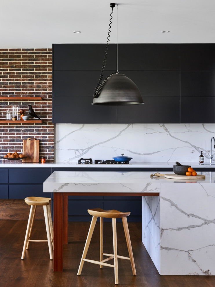Modern inredning av ett vit vitt kök, med bänkskiva i kvarts, släta luckor, svarta skåp, vitt stänkskydd, stänkskydd i sten, mellanmörkt trägolv, en köksö och brunt golv