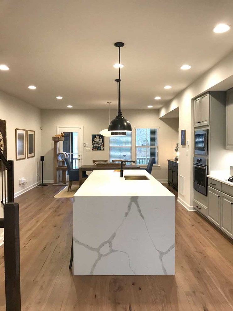 Photo of a small contemporary single-wall kitchen/diner in DC Metro with a submerged sink, white splashback, stainless steel appliances, laminate floors, an island, brown floors and white worktops.