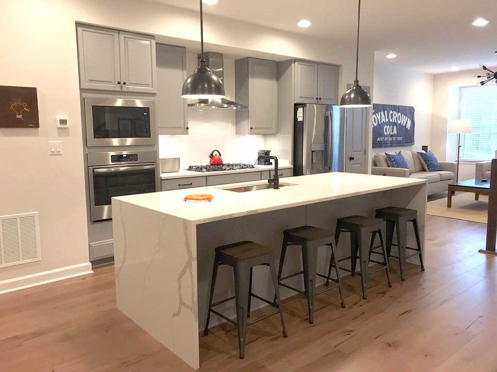 Immagine di una piccola cucina minimal con lavello sottopiano, paraspruzzi bianco, elettrodomestici in acciaio inossidabile, pavimento in laminato, pavimento marrone e top bianco