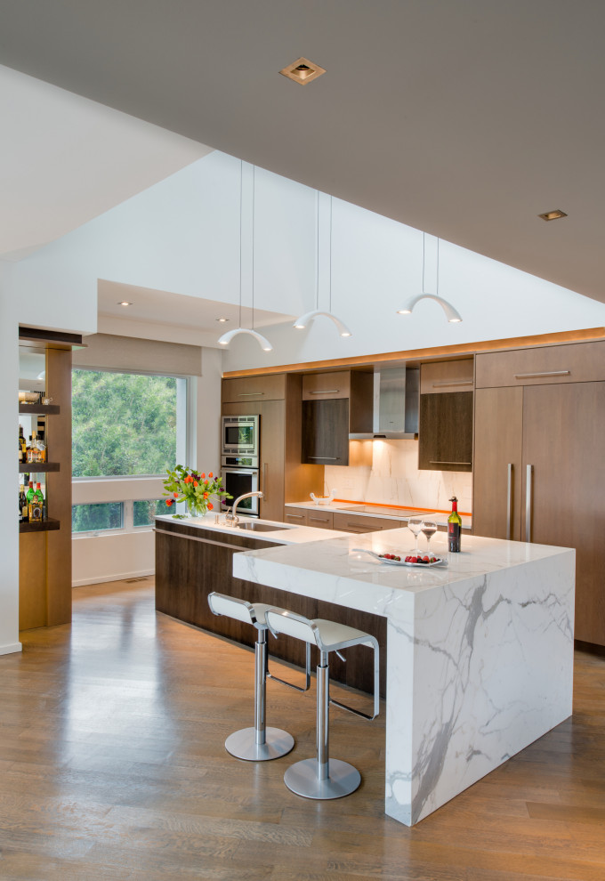 Inspiration for a large contemporary l-shaped kitchen/diner in DC Metro with a submerged sink, flat-panel cabinets, medium wood cabinets, white splashback, integrated appliances, an island, brown floors, white worktops, marble worktops, marble splashback and light hardwood flooring.
