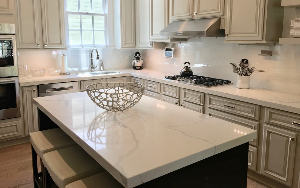 Design ideas for a large traditional l-shaped kitchen/diner in Atlanta with raised-panel cabinets, grey cabinets, engineered stone countertops, white splashback, glass tiled splashback, stainless steel appliances, medium hardwood flooring, an island and brown floors.
