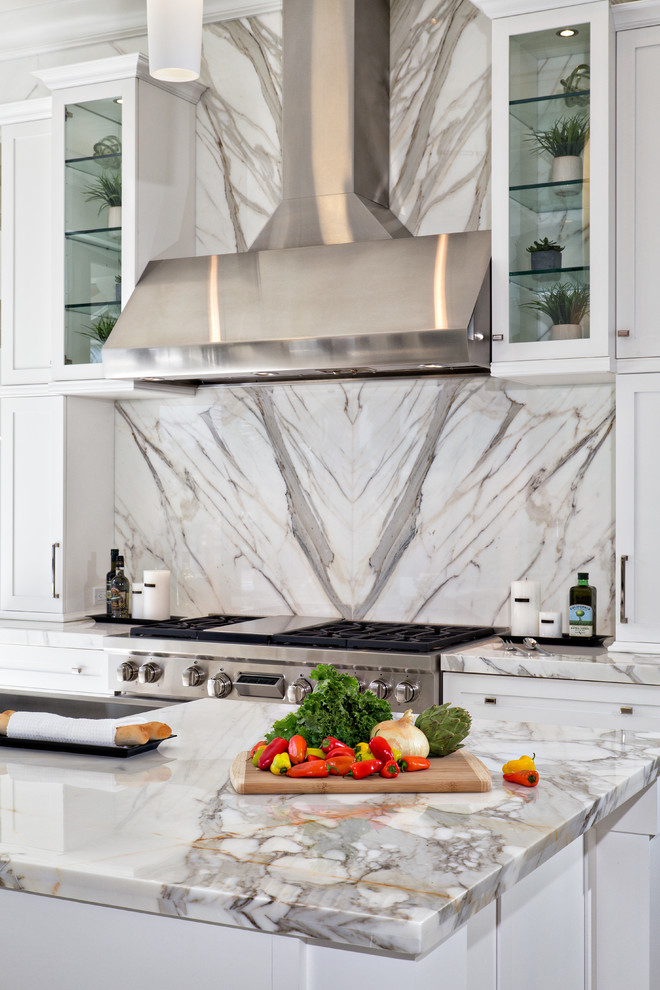 Example of a mid-sized trendy galley marble floor and white floor enclosed kitchen design in Miami with white cabinets, marble countertops, white backsplash, stone slab backsplash, stainless steel appliances, an undermount sink, shaker cabinets and an island
