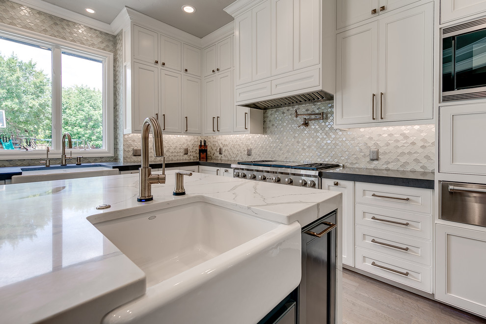 Mid-sized transitional l-shaped light wood floor eat-in kitchen photo in Austin with a farmhouse sink, flat-panel cabinets, white cabinets, quartz countertops, white backsplash, mosaic tile backsplash, stainless steel appliances and an island