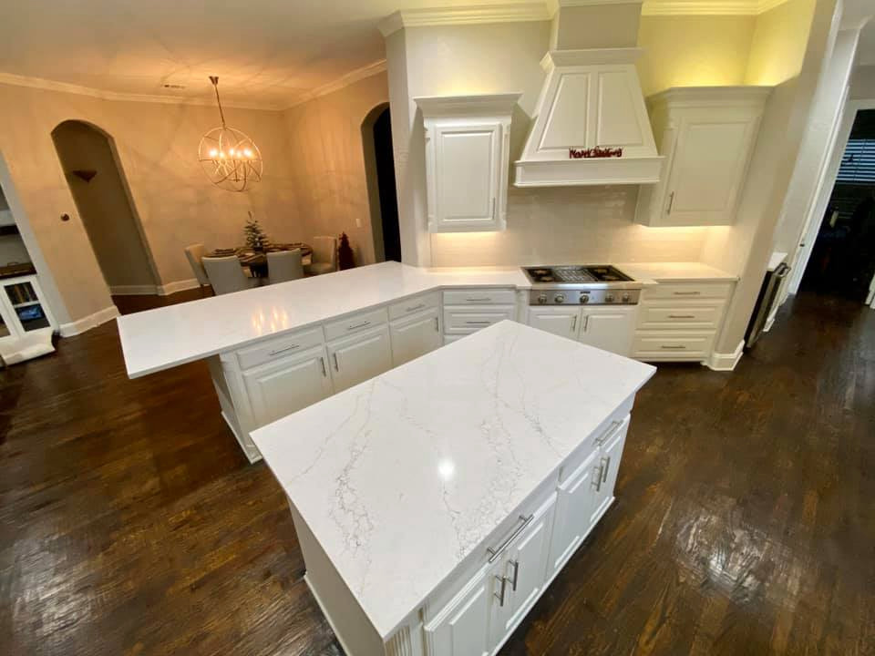 Foto på ett stort vintage vit kök, med en enkel diskho, vita skåp, bänkskiva i kvarts, vitt stänkskydd, stänkskydd i keramik, rostfria vitvaror, mörkt trägolv, en köksö och brunt golv