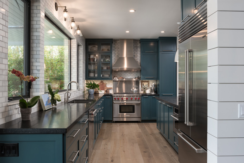 Design ideas for a medium sized classic galley open plan kitchen in San Diego with shaker cabinets, blue cabinets, granite worktops, a breakfast bar, a submerged sink, grey splashback, metro tiled splashback, stainless steel appliances, medium hardwood flooring and brown floors.