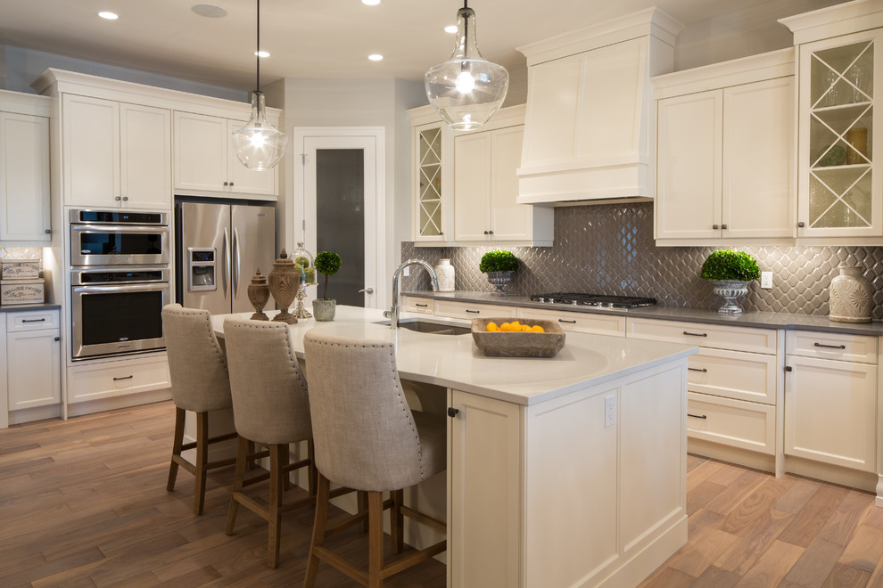 Design ideas for a large classic l-shaped kitchen/diner in Calgary with a submerged sink, shaker cabinets, white cabinets, quartz worktops, grey splashback, ceramic splashback, stainless steel appliances, light hardwood flooring and an island.