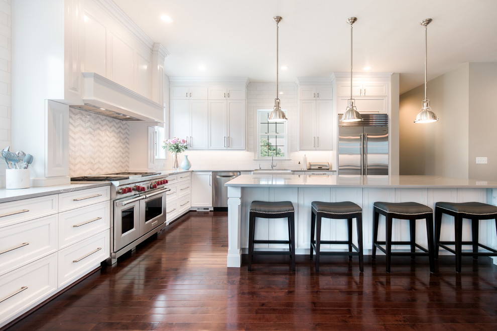 Enclosed kitchen - mid-sized transitional l-shaped dark wood floor and brown floor enclosed kitchen idea in DC Metro with a farmhouse sink, recessed-panel cabinets, white cabinets, quartz countertops, white backsplash, marble backsplash, stainless steel appliances, an island and gray countertops