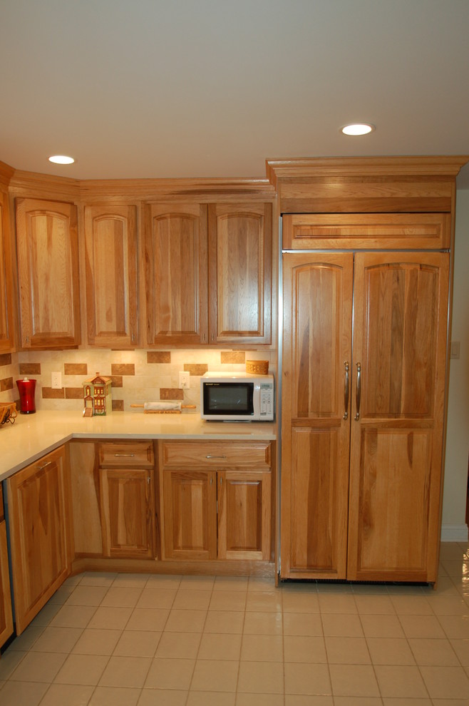 Example of a mid-sized classic l-shaped ceramic tile and beige floor enclosed kitchen design in Newark with an undermount sink, raised-panel cabinets, medium tone wood cabinets, solid surface countertops, beige backsplash, stone tile backsplash, paneled appliances and no island
