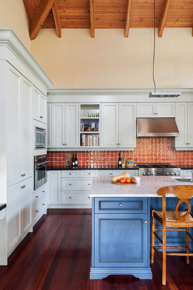 トロントにあるトラディショナルスタイルのおしゃれなキッチン (落し込みパネル扉のキャビネット、オレンジのキッチンパネル、シルバーの調理設備、青いキャビネット) の写真