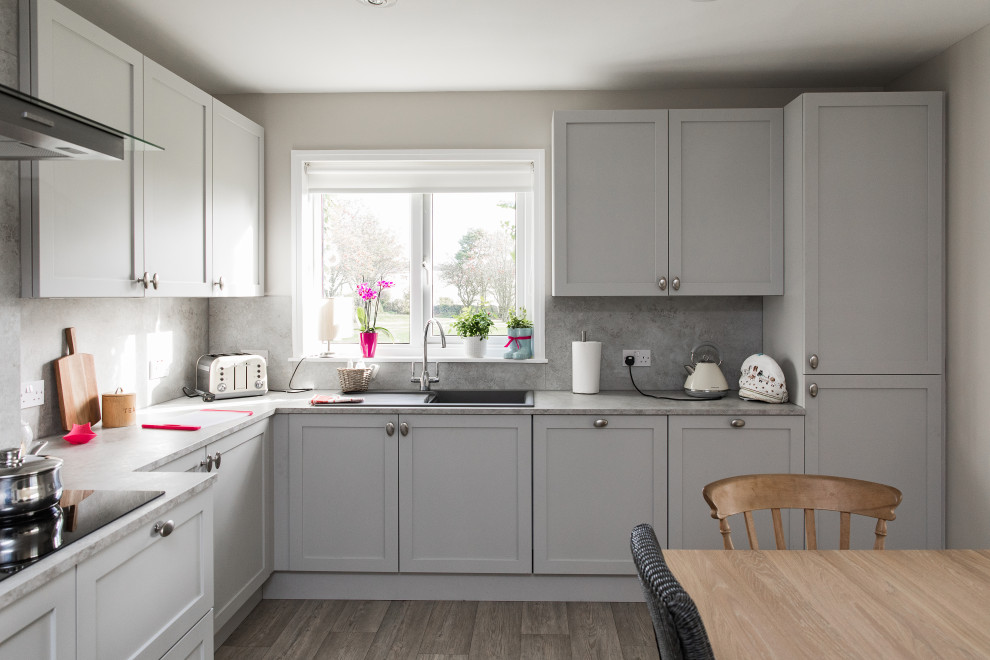 Photo of a medium sized classic l-shaped kitchen/diner in Other with a built-in sink, shaker cabinets, grey cabinets, grey splashback, black appliances, no island, grey floors and grey worktops.