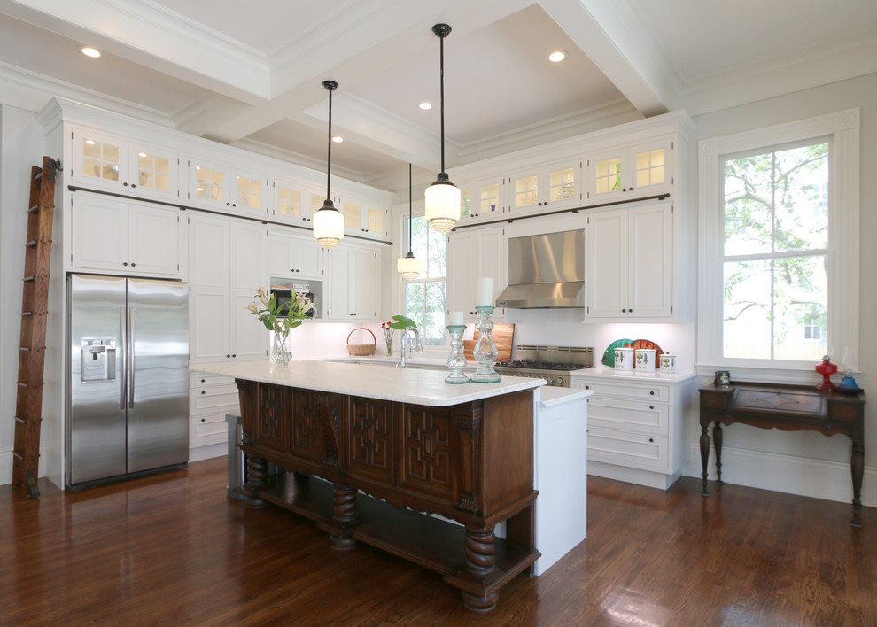 Open concept kitchen - large transitional l-shaped dark wood floor and brown floor open concept kitchen idea in New Orleans with an undermount sink, recessed-panel cabinets, white cabinets, marble countertops, white backsplash, stainless steel appliances and an island