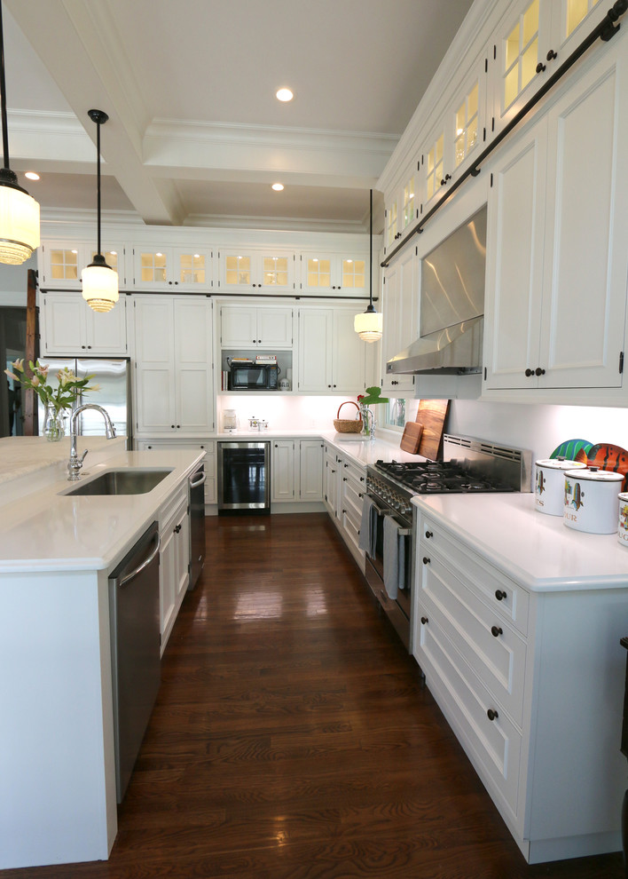 Bild på ett stort vintage kök, med en undermonterad diskho, luckor med infälld panel, vita skåp, marmorbänkskiva, vitt stänkskydd, rostfria vitvaror, mörkt trägolv, en köksö och brunt golv