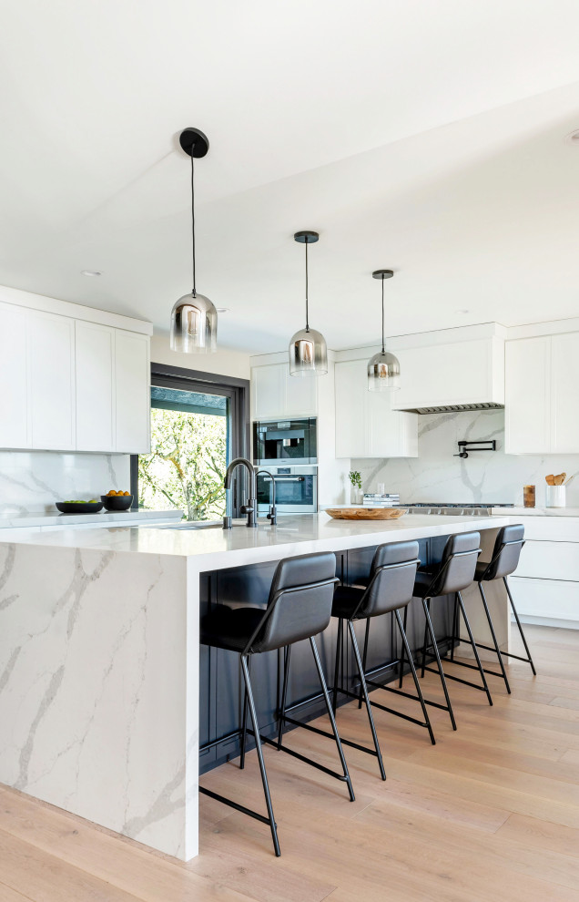 Idées déco pour une grande cuisine contemporaine en L avec un évier encastré, un placard à porte shaker, des portes de placard blanches, une crédence blanche, un électroménager en acier inoxydable, îlot, un sol beige et un plan de travail blanc.