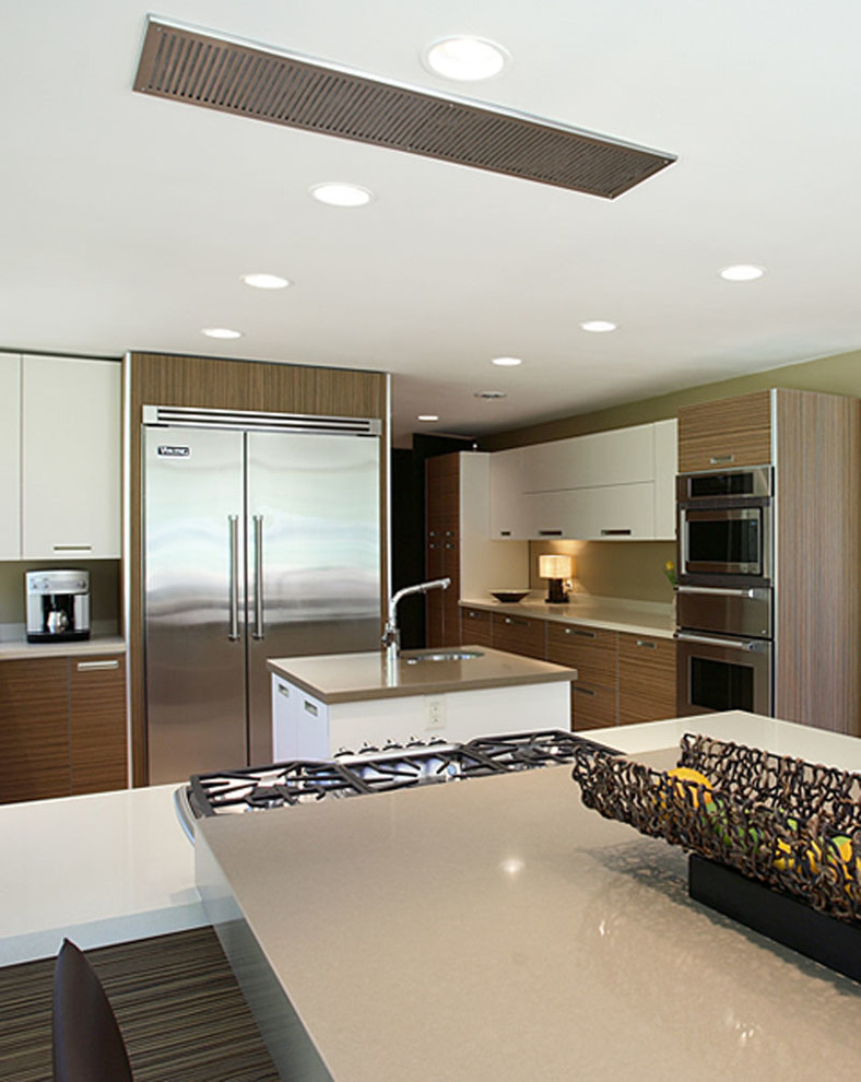 Modern inredning av ett stort kök, med en undermonterad diskho, skåp i mellenmörkt trä, rostfria vitvaror och en köksö