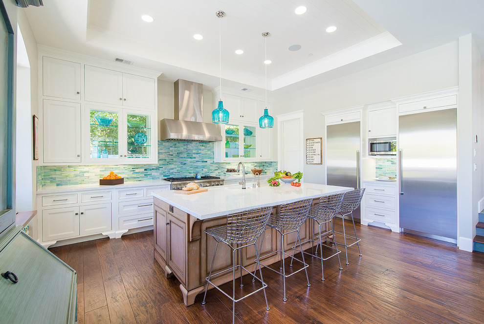 Example of a large beach style l-shaped dark wood floor and brown floor open concept kitchen design in Los Angeles with recessed-panel cabinets, white cabinets, multicolored backsplash, stainless steel appliances, an island, quartz countertops, mosaic tile backsplash, an undermount sink and white countertops