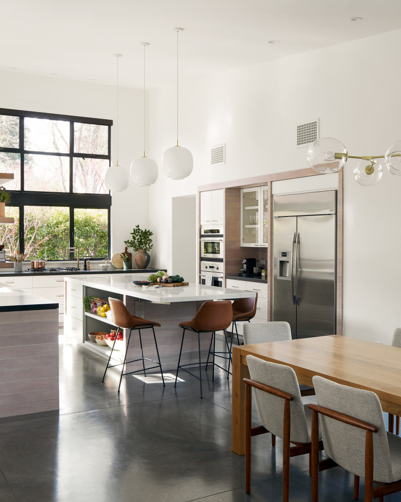 Foto på ett minimalistiskt vit kök, med släta luckor, en köksö, vita skåp, rostfria vitvaror, betonggolv och grått golv
