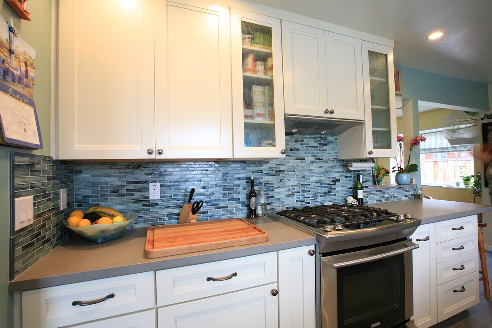 Bild på ett mellanstort maritimt kök, med en undermonterad diskho, luckor med infälld panel, vita skåp, bänkskiva i kvarts, blått stänkskydd, stänkskydd i glaskakel, rostfria vitvaror och klinkergolv i porslin