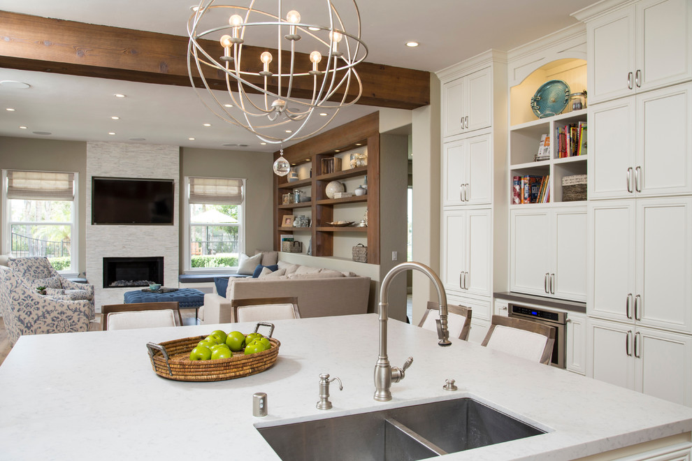 Inspiration for a mid-sized coastal l-shaped light wood floor open concept kitchen remodel in San Diego with a double-bowl sink, recessed-panel cabinets, white cabinets, quartz countertops, white backsplash, stone tile backsplash, stainless steel appliances and an island