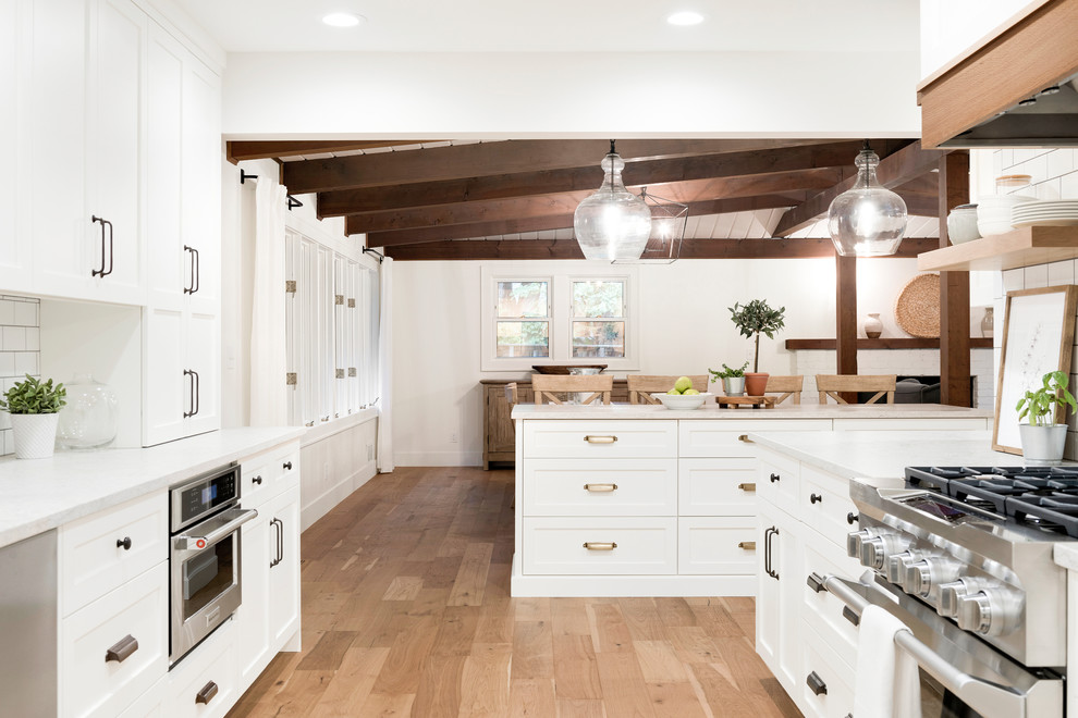Idéer för stora rustika vitt kök och matrum, med en rustik diskho, luckor med profilerade fronter, skåp i ljust trä, vitt stänkskydd, stänkskydd i keramik, rostfria vitvaror, ljust trägolv, en köksö och beiget golv
