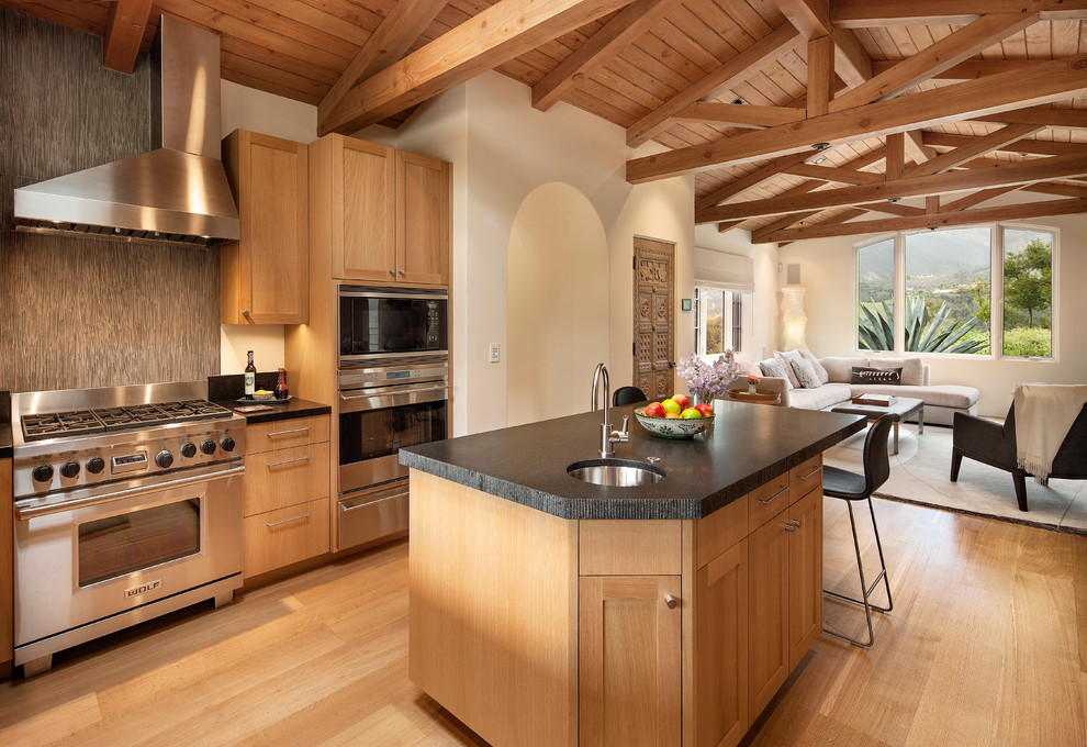 На фото: кухня-гостиная в средиземноморском стиле с фасадами в стиле шейкер, светлыми деревянными фасадами и техникой из нержавеющей стали