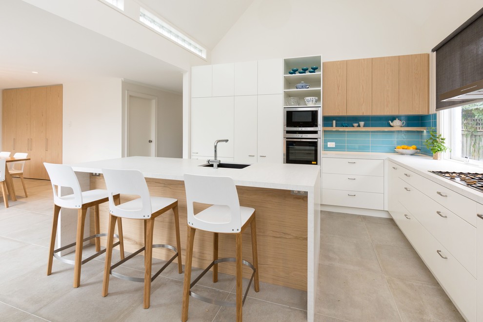 Foto på ett funkis kök, med en undermonterad diskho, släta luckor, vita skåp, blått stänkskydd, rostfria vitvaror och en köksö