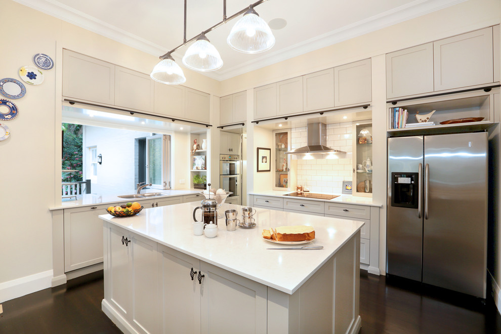 Moderne Küche in L-Form mit Doppelwaschbecken, Schrankfronten im Shaker-Stil, beigen Schränken, Küchenrückwand in Weiß, Rückwand aus Metrofliesen, Küchengeräten aus Edelstahl, dunklem Holzboden und Kücheninsel in Sydney
