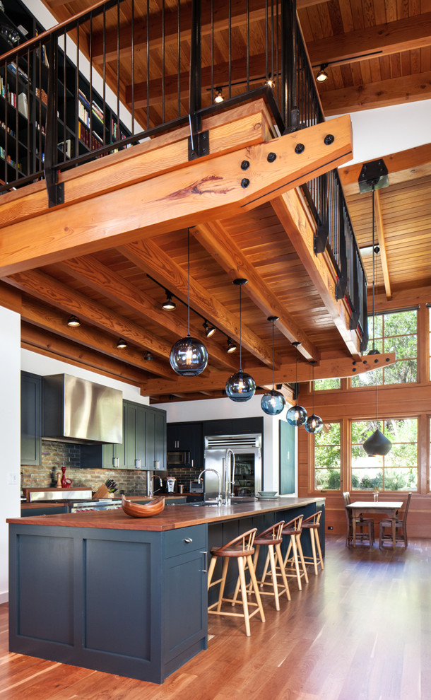 Cette image montre une cuisine ouverte parallèle chalet avec un placard à porte shaker, des portes de placard bleues, un plan de travail en bois, un électroménager en acier inoxydable, un sol en bois brun et îlot.