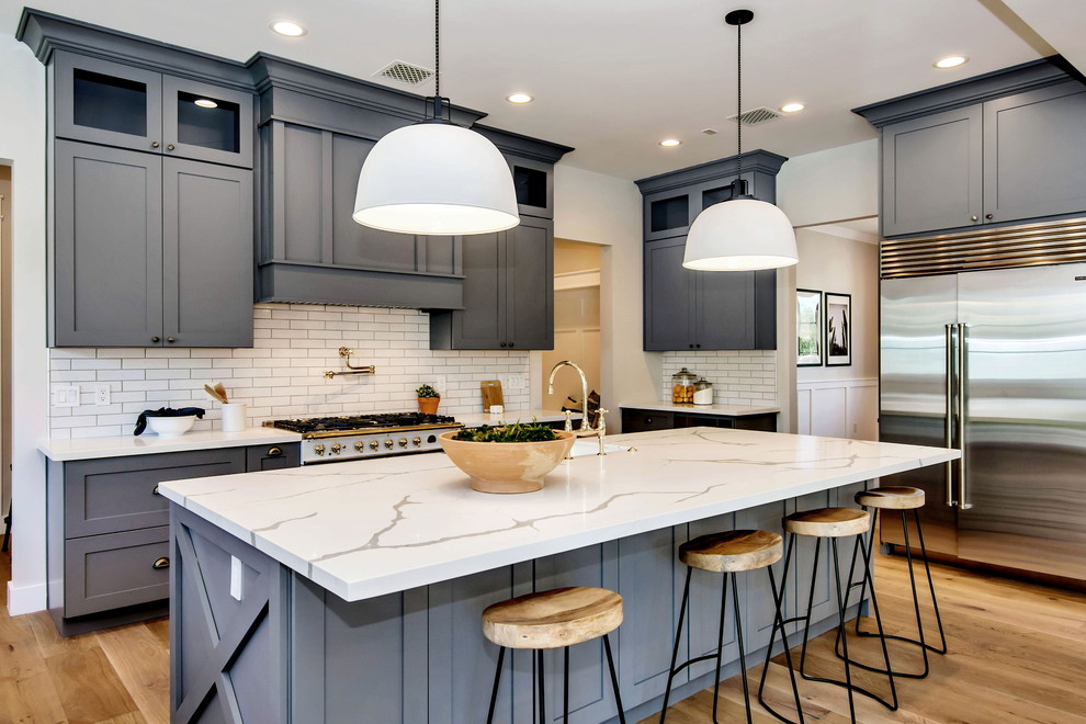 Inspiration for a large craftsman single-wall light wood floor and brown floor open concept kitchen remodel in Phoenix with a farmhouse sink, shaker cabinets, gray cabinets, quartzite countertops, white backsplash, subway tile backsplash, stainless steel appliances, an island and white countertops