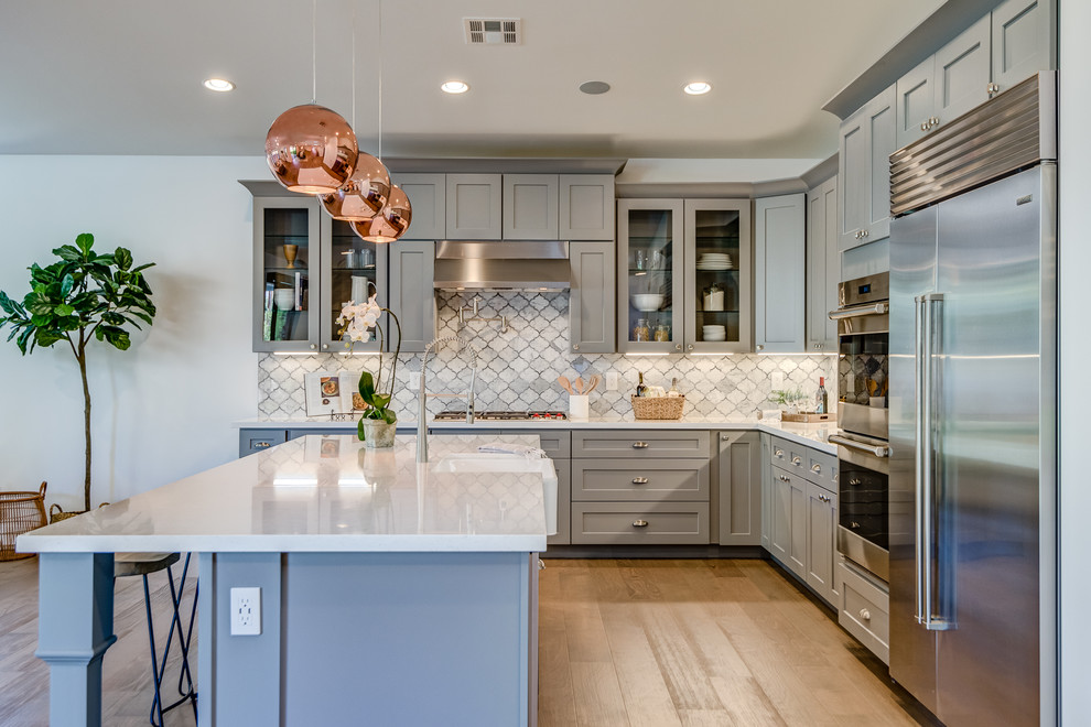 Inspiration for a large transitional l-shaped brown floor and medium tone wood floor open concept kitchen remodel in Phoenix with gray cabinets, gray backsplash, an island, white countertops, a farmhouse sink, shaker cabinets and stainless steel appliances