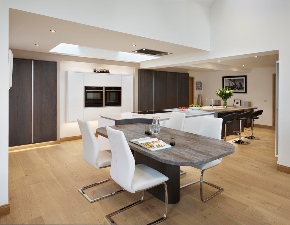 Foto di una grande cucina minimal con ante lisce, elettrodomestici in acciaio inossidabile, parquet chiaro, pavimento beige e top bianco