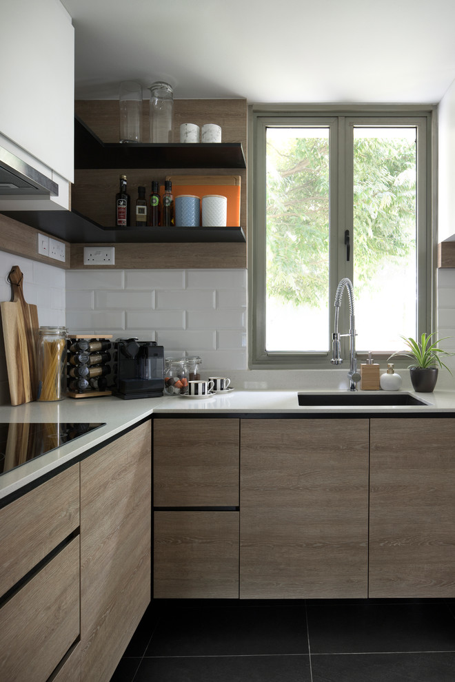 Photo of a contemporary l-shaped kitchen in Singapore with a submerged sink, flat-panel cabinets, light wood cabinets, white splashback, metro tiled splashback, black floors and white worktops.