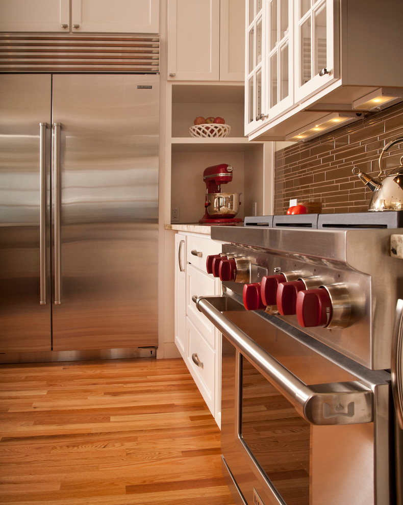 Klassisk inredning av ett mellanstort kök, med en undermonterad diskho, vita skåp, marmorbänkskiva, brunt stänkskydd, rostfria vitvaror, mellanmörkt trägolv, en köksö, luckor med glaspanel och stänkskydd i stickkakel