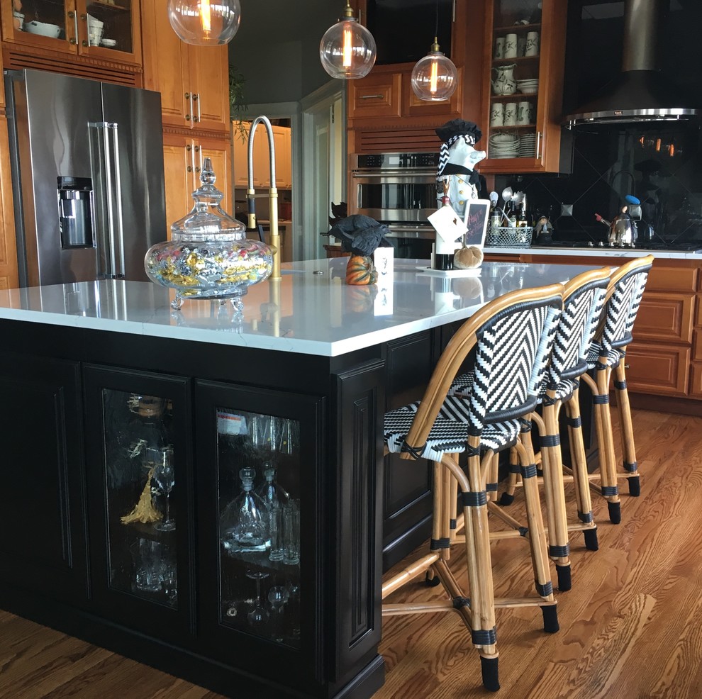 シアトルにある高級な中くらいなトランジショナルスタイルのおしゃれなキッチン (エプロンフロントシンク、レイズドパネル扉のキャビネット、クオーツストーンカウンター、黒いキッチンパネル、石タイルのキッチンパネル、シルバーの調理設備、無垢フローリング、茶色い床、中間色木目調キャビネット、白いキッチンカウンター) の写真
