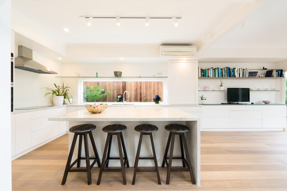 Moderne Küche mit flächenbündigen Schrankfronten, weißen Schränken, Küchenrückwand in Weiß, Küchengeräten aus Edelstahl, hellem Holzboden und Kücheninsel in Melbourne