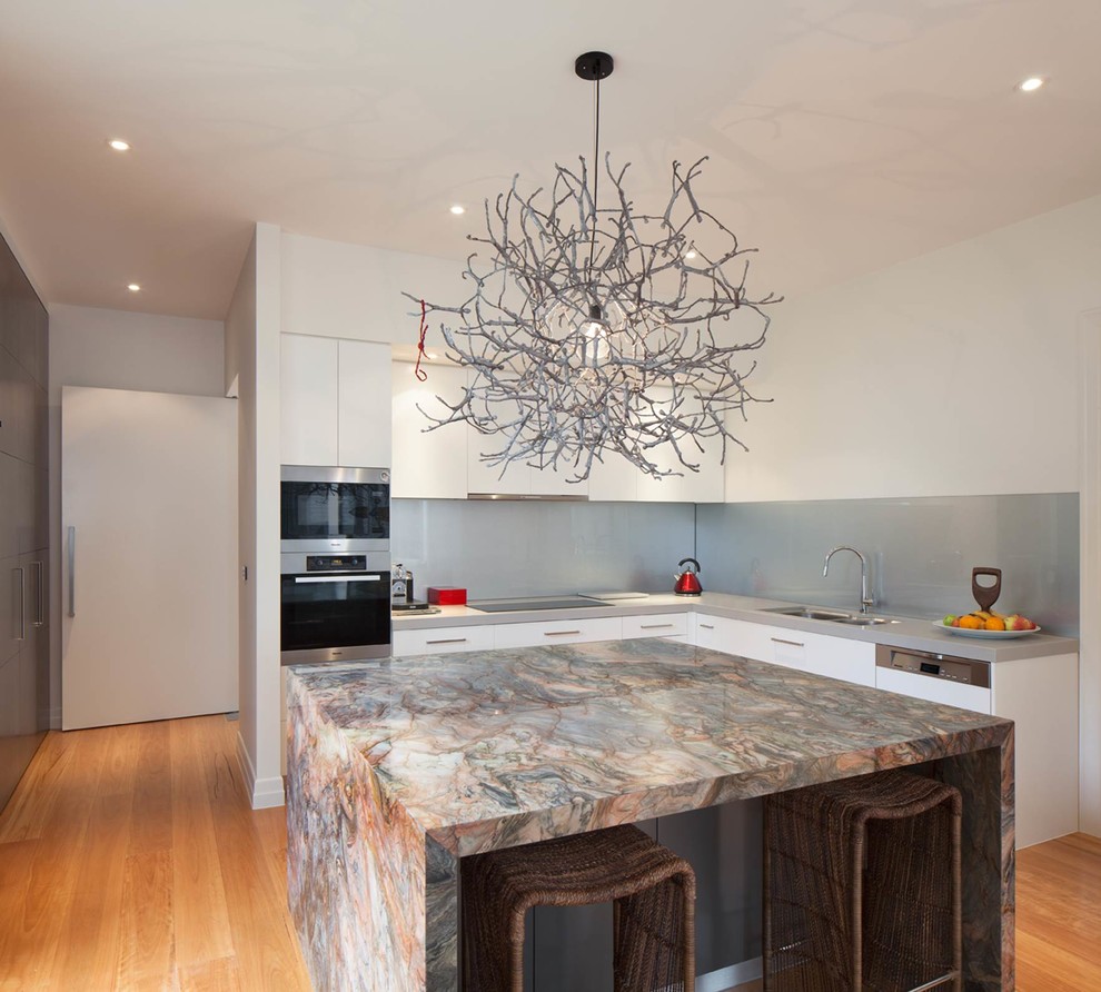 Modern inredning av ett mellanstort l-kök, med en undermonterad diskho, släta luckor, vita skåp, marmorbänkskiva, grått stänkskydd, rostfria vitvaror, mellanmörkt trägolv och en köksö