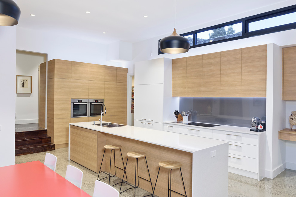 Example of a large trendy galley concrete floor eat-in kitchen design in Melbourne with an integrated sink, flat-panel cabinets, light wood cabinets, quartz countertops, black backsplash, glass sheet backsplash, stainless steel appliances and an island