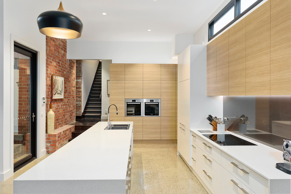 Große Moderne Küche mit flächenbündigen Schrankfronten, hellen Holzschränken, Quarzwerkstein-Arbeitsplatte, Glasrückwand, Küchengeräten aus Edelstahl, Kücheninsel und Doppelwaschbecken in Melbourne