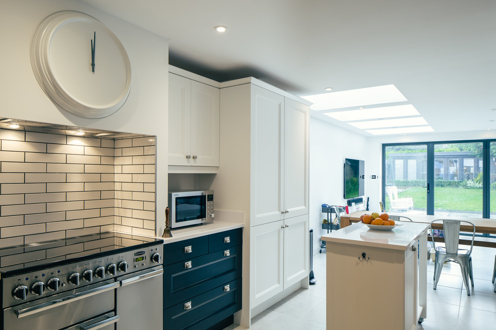 Modern inredning av ett mellanstort kök, med en nedsänkt diskho, skåp i shakerstil, blå skåp, granitbänkskiva, vitt stänkskydd, glaspanel som stänkskydd, rostfria vitvaror, skiffergolv, en köksö och beiget golv
