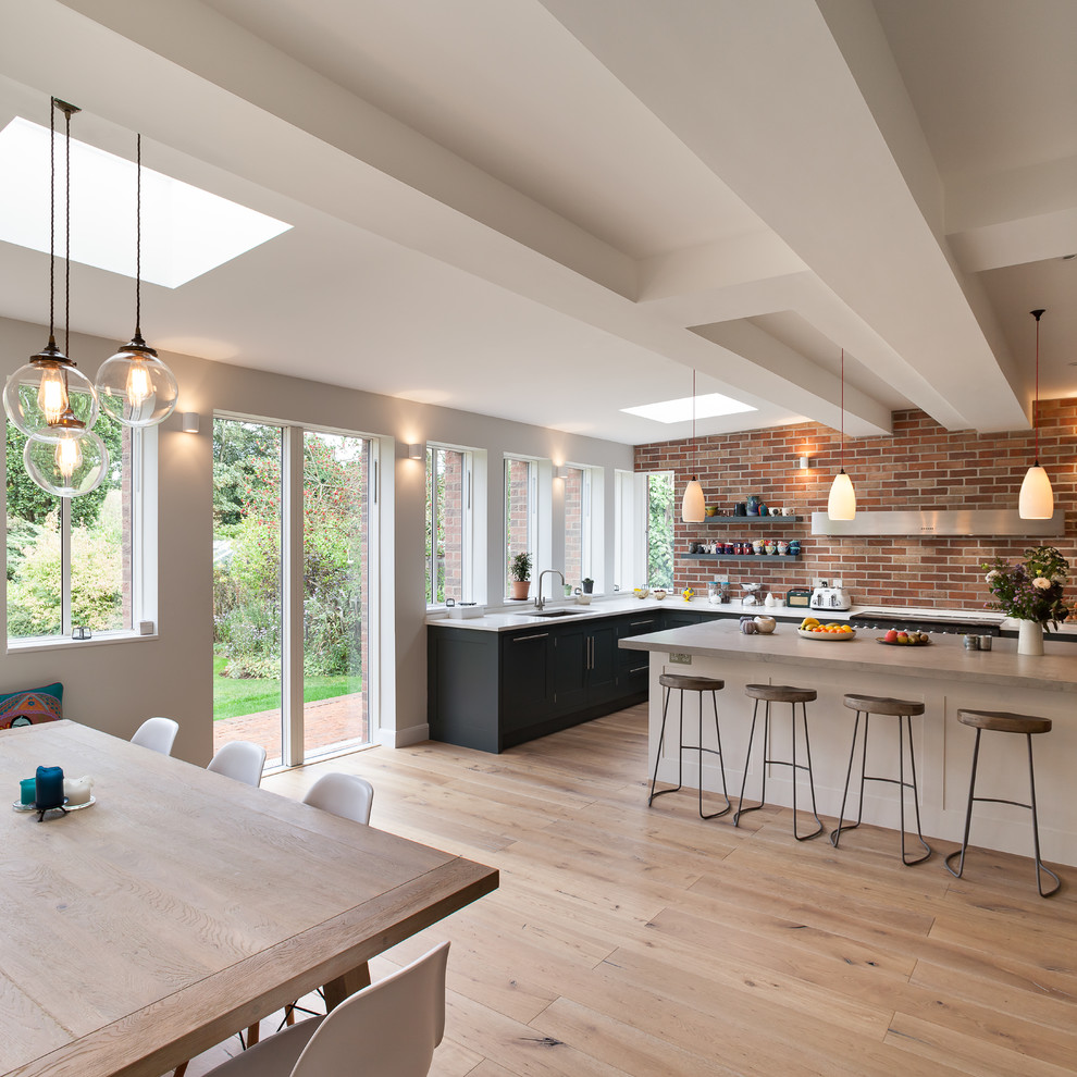 Large contemporary l-shaped kitchen/diner in Cambridgeshire with a built-in sink, recessed-panel cabinets, grey cabinets, composite countertops, integrated appliances, light hardwood flooring, an island and white worktops.
