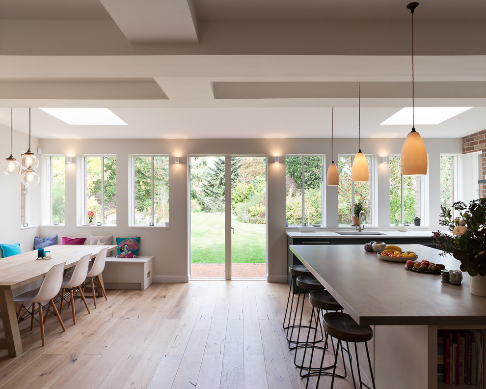 Photo of a large contemporary l-shaped kitchen/diner in Cambridgeshire with a built-in sink, recessed-panel cabinets, grey cabinets, composite countertops, integrated appliances, light hardwood flooring, an island and white worktops.