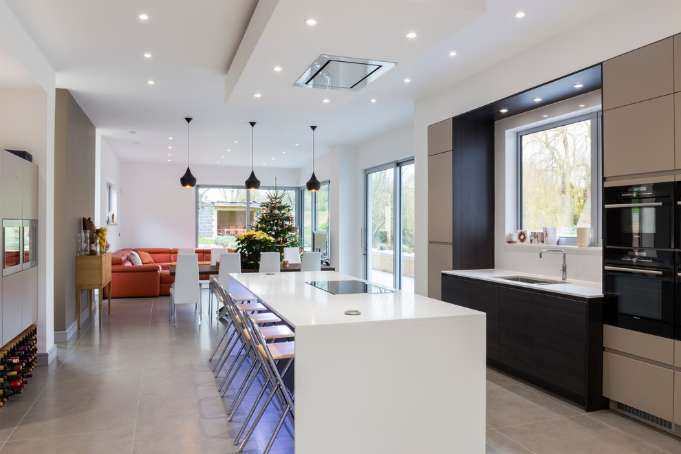 This is an example of a contemporary open plan kitchen in London with a submerged sink, flat-panel cabinets, grey cabinets, black appliances and an island.
