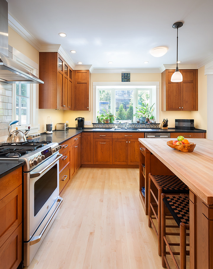Inspiration for a mid-sized transitional u-shaped light wood floor kitchen remodel in Boston with an undermount sink, shaker cabinets, medium tone wood cabinets, ceramic backsplash, stainless steel appliances and an island