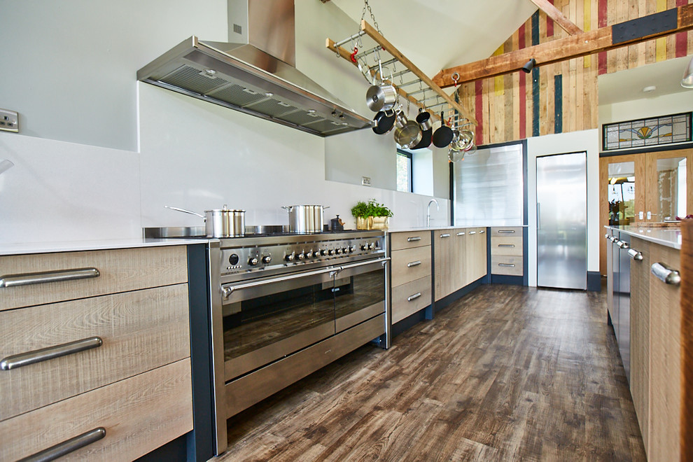 Foto på ett stort industriellt vit kök, med en undermonterad diskho, släta luckor, skåp i ljust trä, granitbänkskiva, vitt stänkskydd, glaspanel som stänkskydd, rostfria vitvaror, mellanmörkt trägolv, en köksö och brunt golv