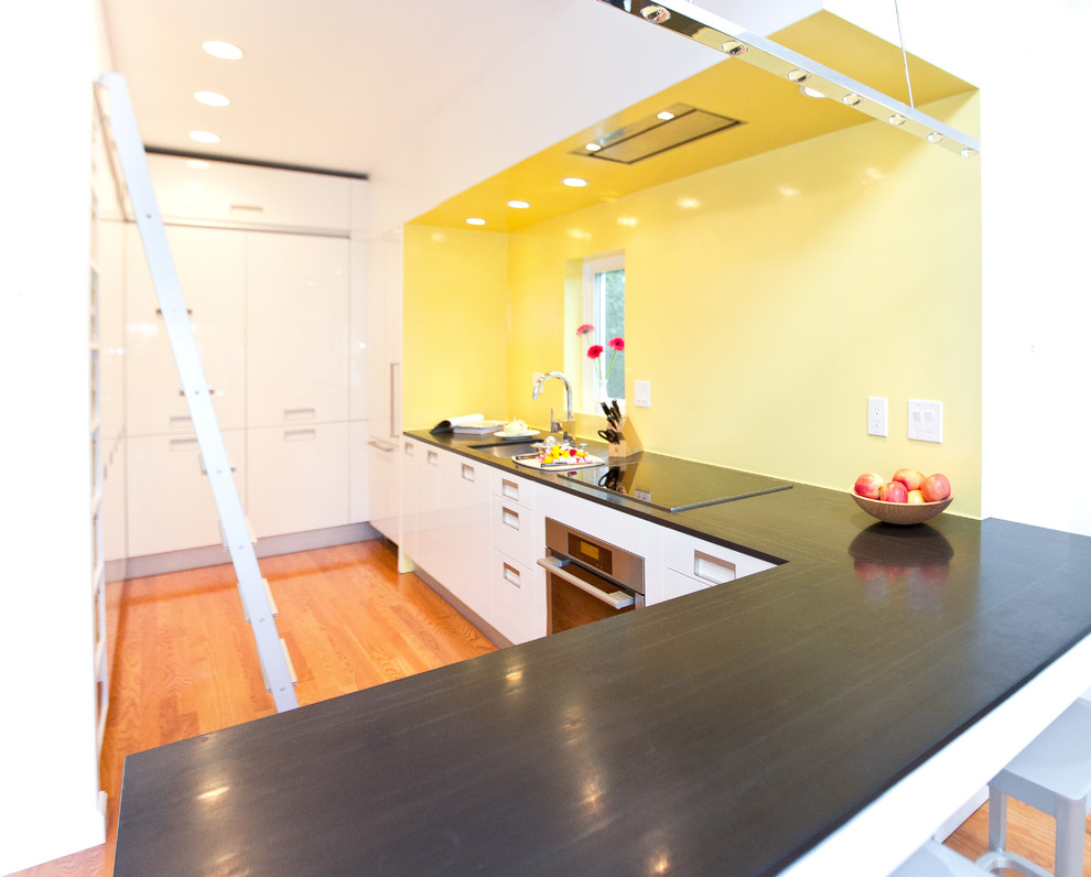 Moderne Wohnküche in U-Form mit Unterbauwaschbecken, flächenbündigen Schrankfronten, weißen Schränken, Speckstein-Arbeitsplatte, Küchenrückwand in Gelb und weißen Elektrogeräten in Boston