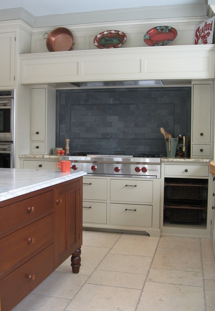 This is an example of a medium sized traditional l-shaped enclosed kitchen in Portland Maine with a belfast sink, shaker cabinets, white cabinets, marble worktops, grey splashback, stone tiled splashback, stainless steel appliances, travertine flooring and an island.
