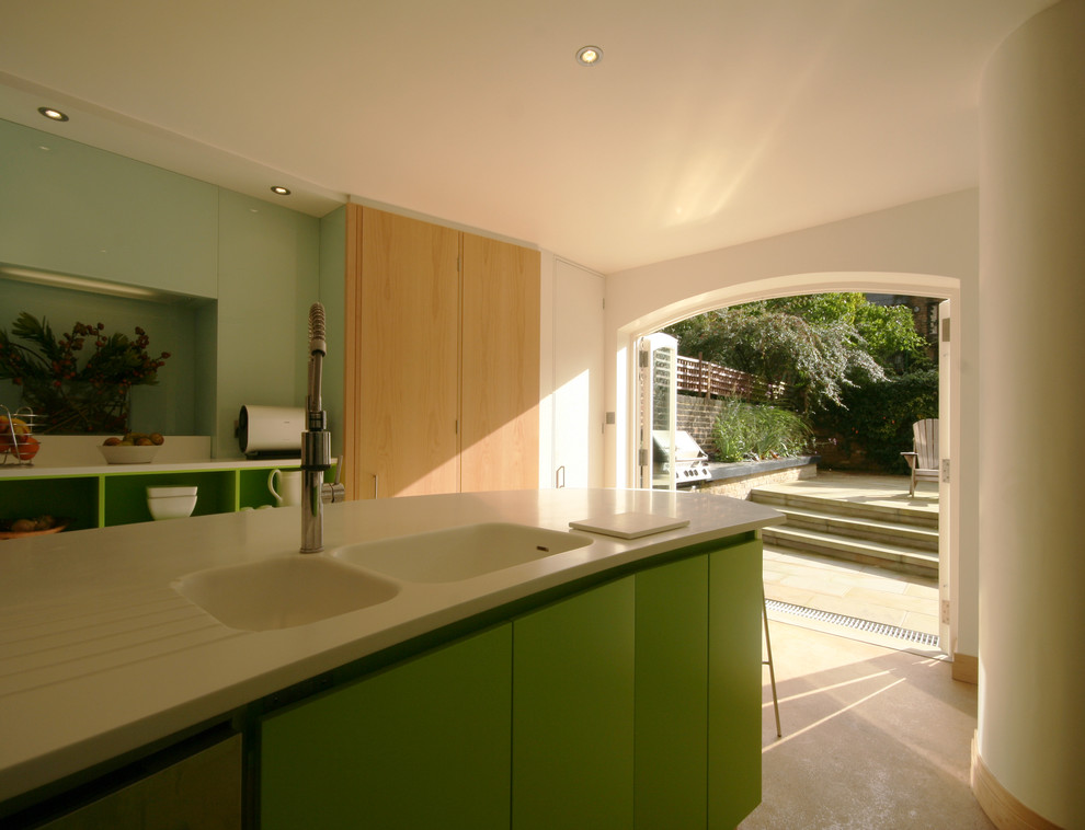 Moderne Küche mit flächenbündigen Schrankfronten, grünen Schränken, Glasrückwand, Betonboden, Kücheninsel, Mineralwerkstoff-Arbeitsplatte und integriertem Waschbecken in London