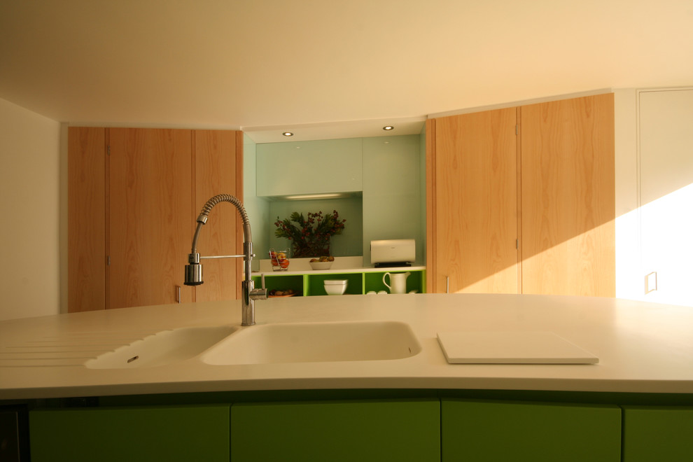 Imagen de cocina minimalista con armarios con paneles lisos, puertas de armario de madera clara, salpicadero de vidrio templado, una isla, fregadero integrado y encimera de acrílico
