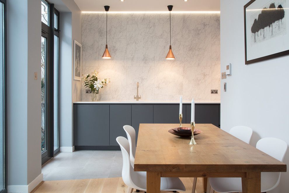 Design ideas for a large contemporary galley open plan kitchen in London with an integrated sink, flat-panel cabinets, grey cabinets, composite countertops, white splashback, stone tiled splashback, black appliances, concrete flooring and grey floors.