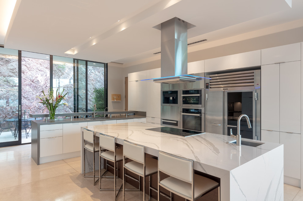 Eat-in kitchen - contemporary u-shaped travertine floor and beige floor eat-in kitchen idea in Phoenix with an undermount sink, flat-panel cabinets, white cabinets, quartzite countertops, stainless steel appliances, an island and white countertops